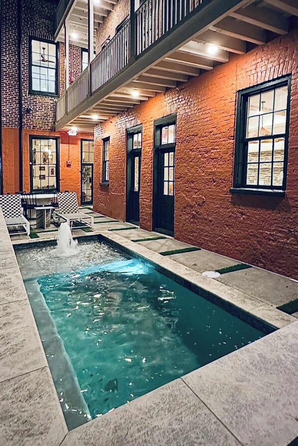 Une piscine intérieure dotée d’une fontaine, entourée de murs et de fenêtres en briques.