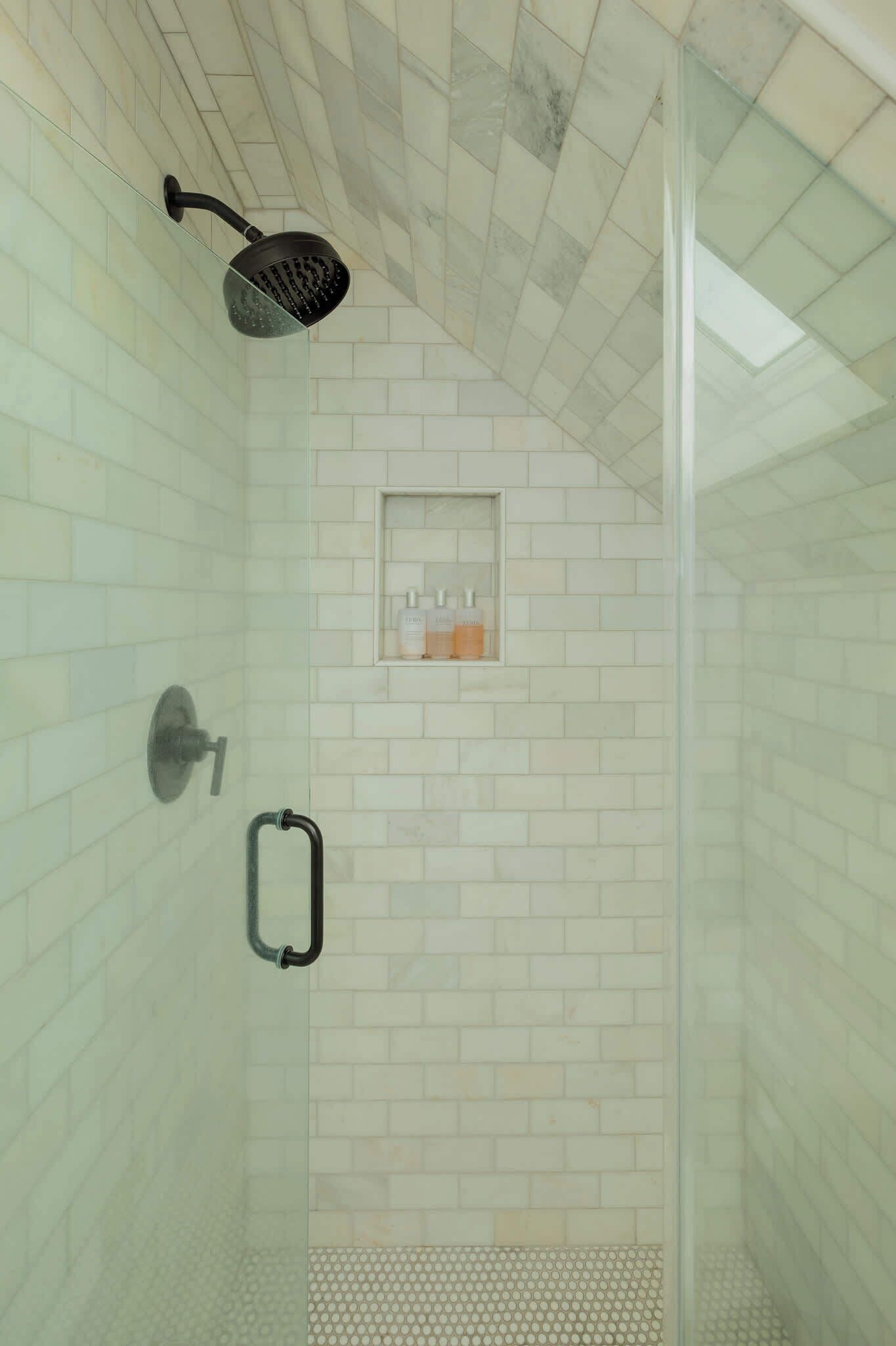 A shower with a glass door, a handheld showerhead, and a small shelf with toiletries.
