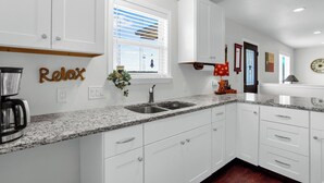 A modern kitchen with white cabinets, granite countertops, a double sink, and a coffee maker. - Clare House I Couples, Stargazing (San Marcos)