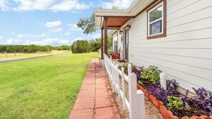 A house with a covered porch, a white fence, and a garden with purple plants. - Clare House I Couples, Stargazing (San Marcos)