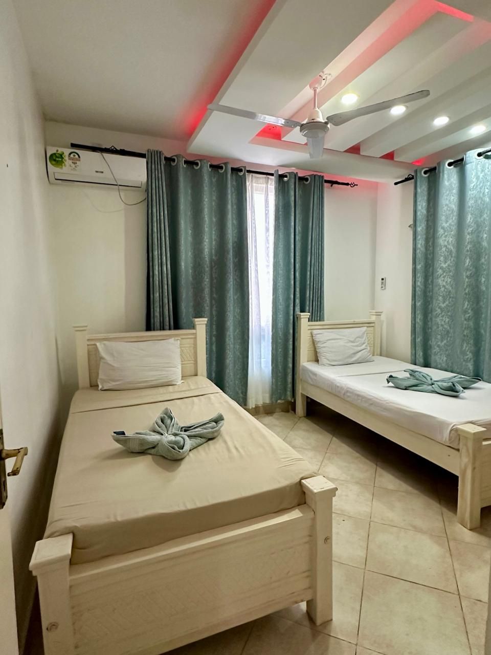 A room with two single beds, a ceiling fan, and a window with curtains.