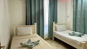 A room with two single beds, a ceiling fan, and a window with curtains.