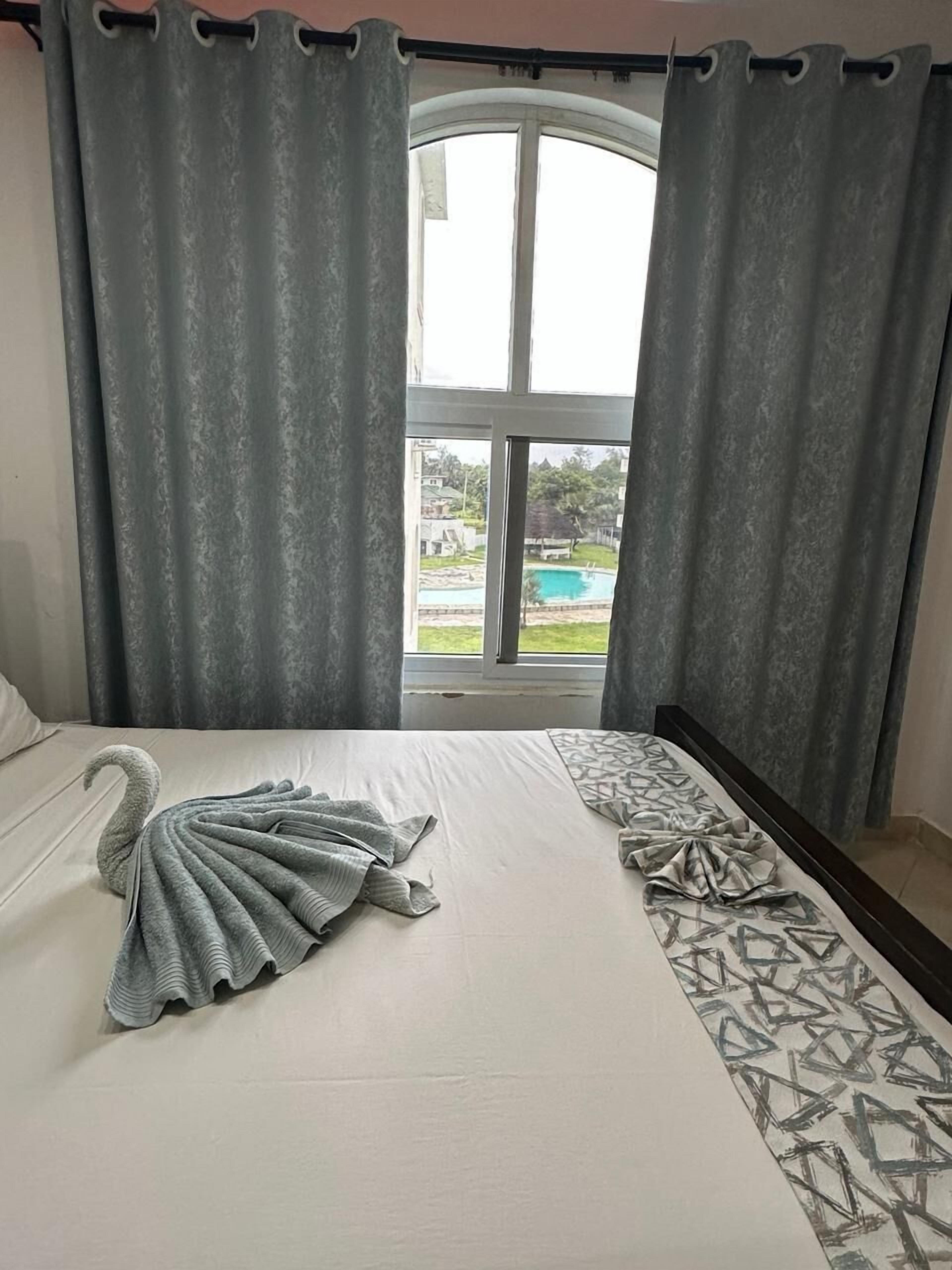 Et hotelværelse med en seng, grå gardiner og udsigt til en swimmingpool.