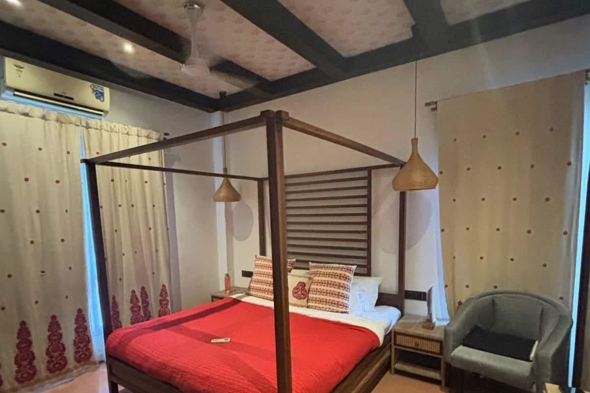 Uma cama de dossel com colcha vermelha, mesa de cabeceira de madeira, uma cadeira e um tapete redondo.