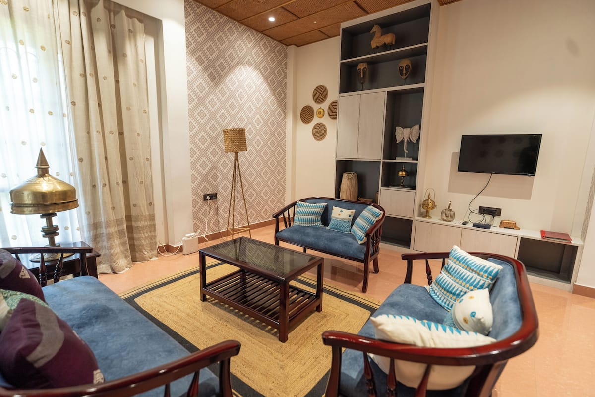 Uma sala de estar com sofá, poltronas, mesa de centro, abajur e televisão.