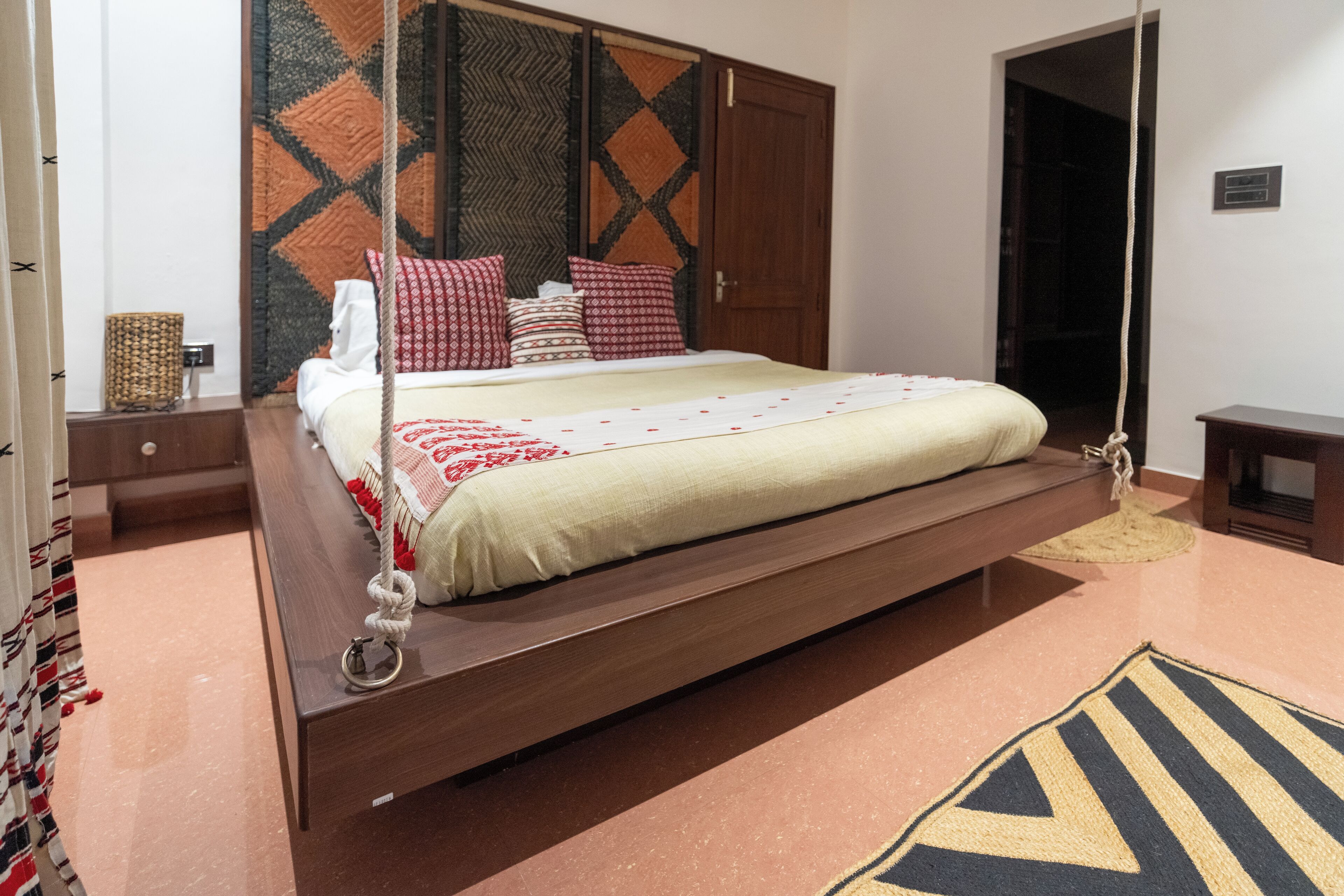 Una cama con estructura de madera, una cuerda colgante y almohadas estampadas.