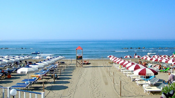 A beach with rows of sun umbrellas and lounge chairs, a lifeguard tower, and the ocean in the background.