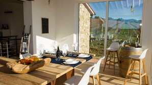 A dining area with a wooden table set for four, white chairs, and a rustic wooden bowl filled with fruits. - Villa Bibbona con Piscina (Bibbona)