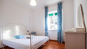 Een slaapkamer met een enkel bed, een dressoir, een spiegel en een raam met gordijnen.