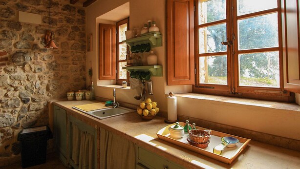 A rustic kitchen with stone walls, wooden beams, a sink, and a window with a view of greenery. - Villa Este con Piscina (Civitella Paganico)