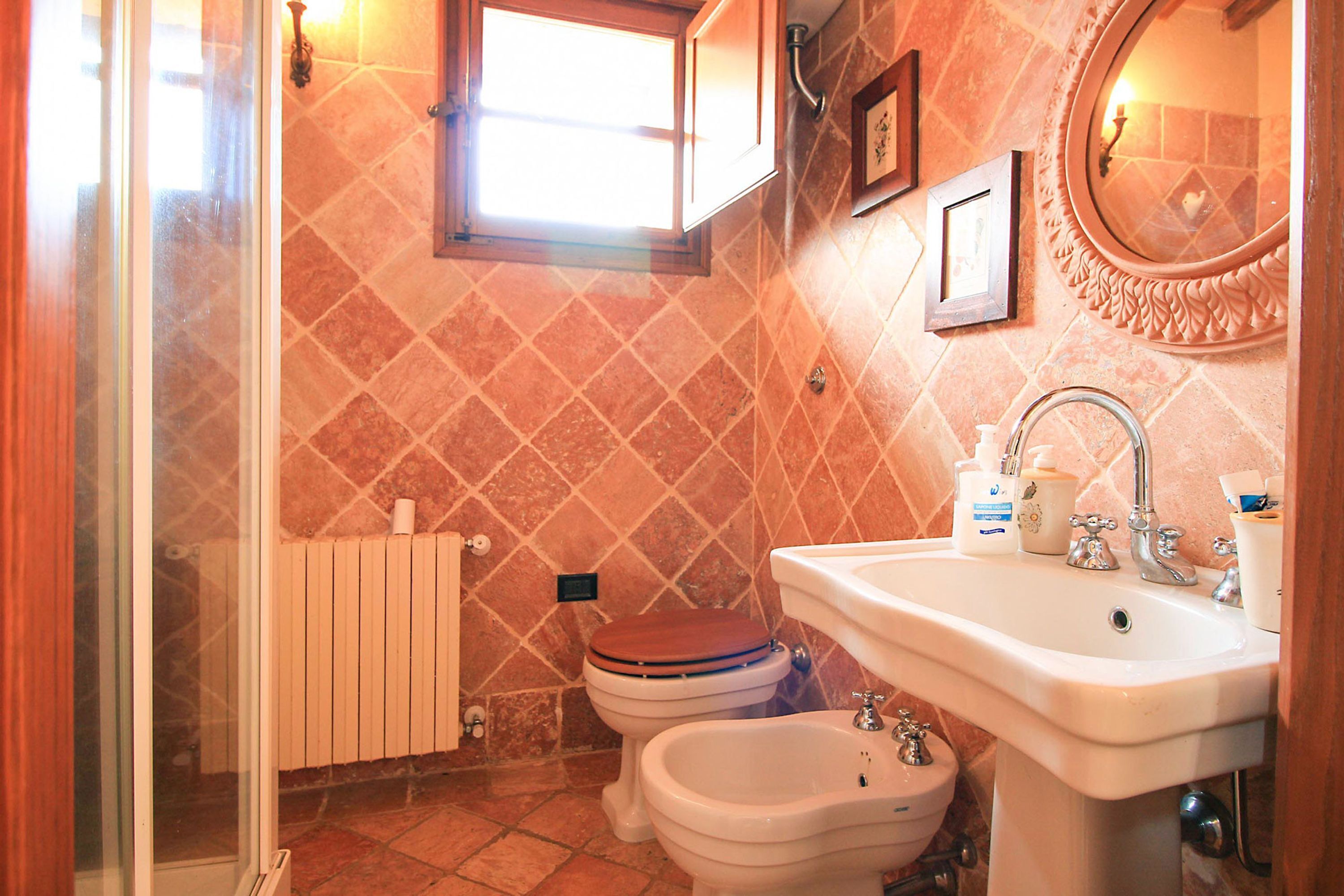 A bathroom with a shower, toilet, bidet, sink, and a window.