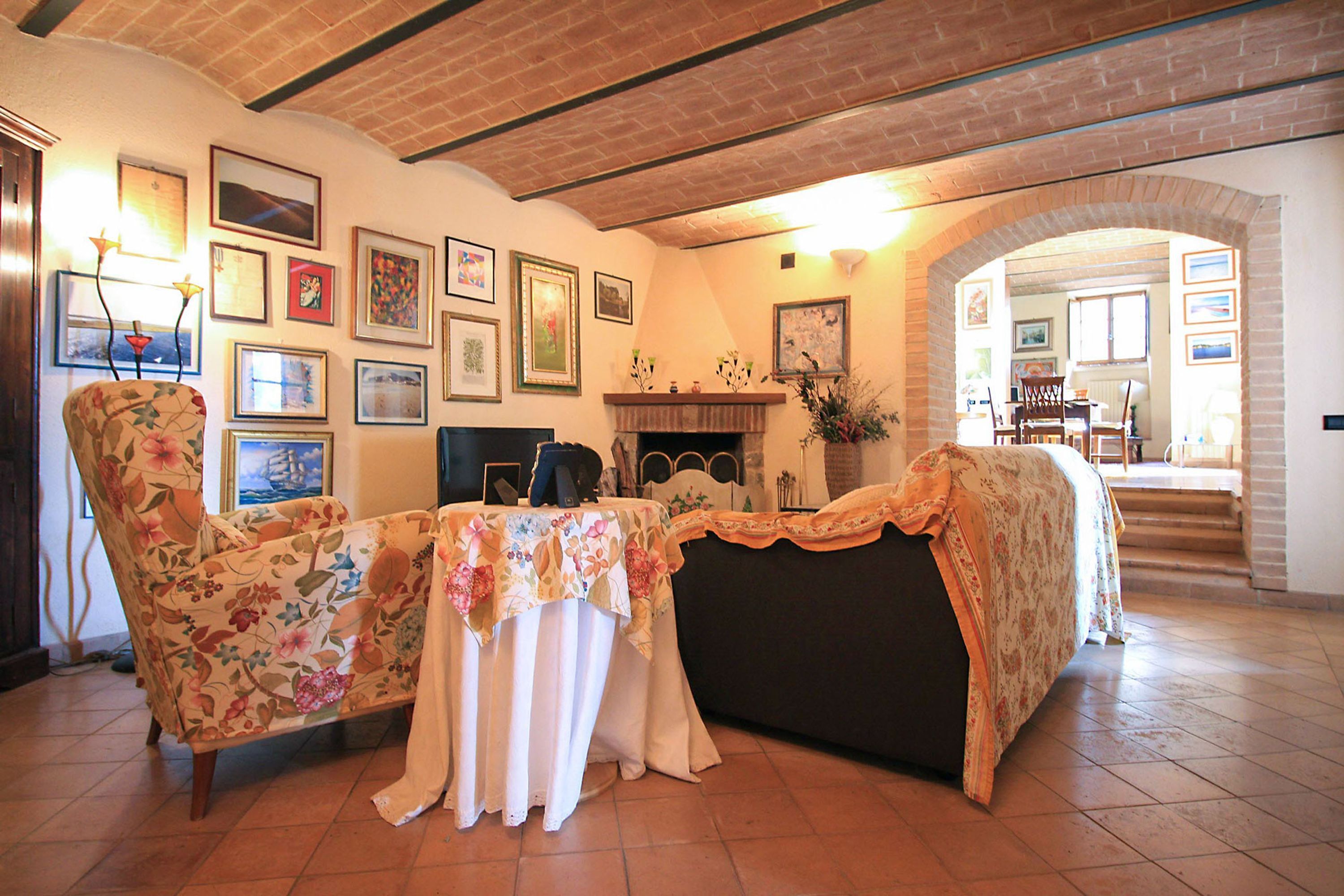 Ein Wohnzimmer mit Kamin, floralen Sesseln, einem Tisch mit Tischdecke und einer Treppe, die in einen anderen Raum führt.
