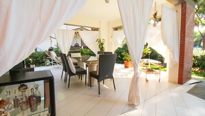 An outdoor patio area with a table and chairs, surrounded by white curtains and potted plants. - Villa Gio-d con Grande Giardino (Grosseto)