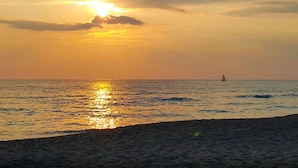 Ein Sonnenuntergang über dem Meer mit einem Segelboot in der Ferne.