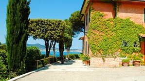 A building with a stone facade and green vines, a paved pathway, and a view of the sea.