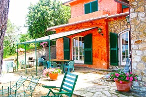 A stone building with a red facade, green shutters, and outdoor seating with chairs and tables. - Villa Stefania Isola d Elba (Portoferraio)
