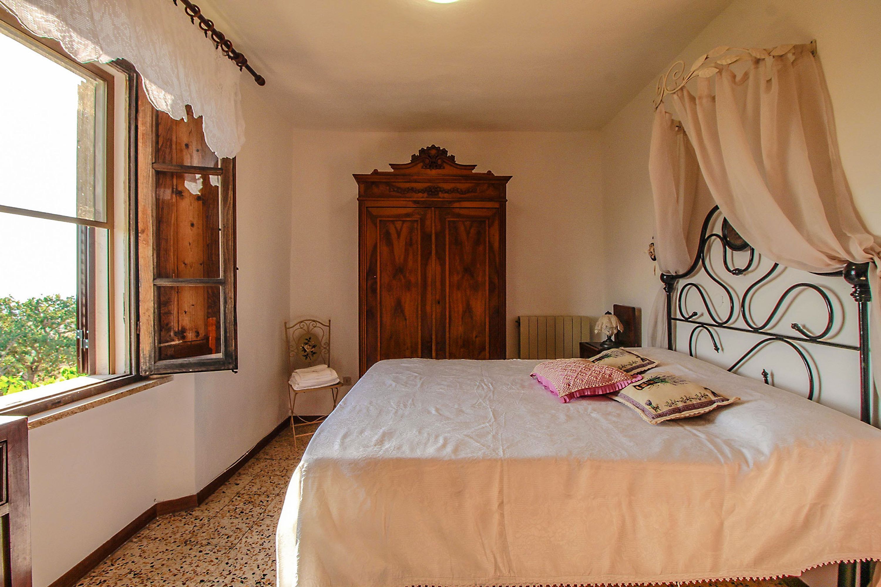 A bedroom with a bed, a wooden wardrobe, a window with lace curtains, and a radiator.