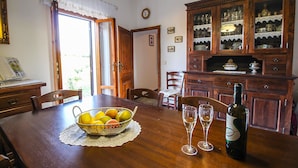 A dining area with a wooden table, a fruit basket, two wine glasses, and a wine bottle.