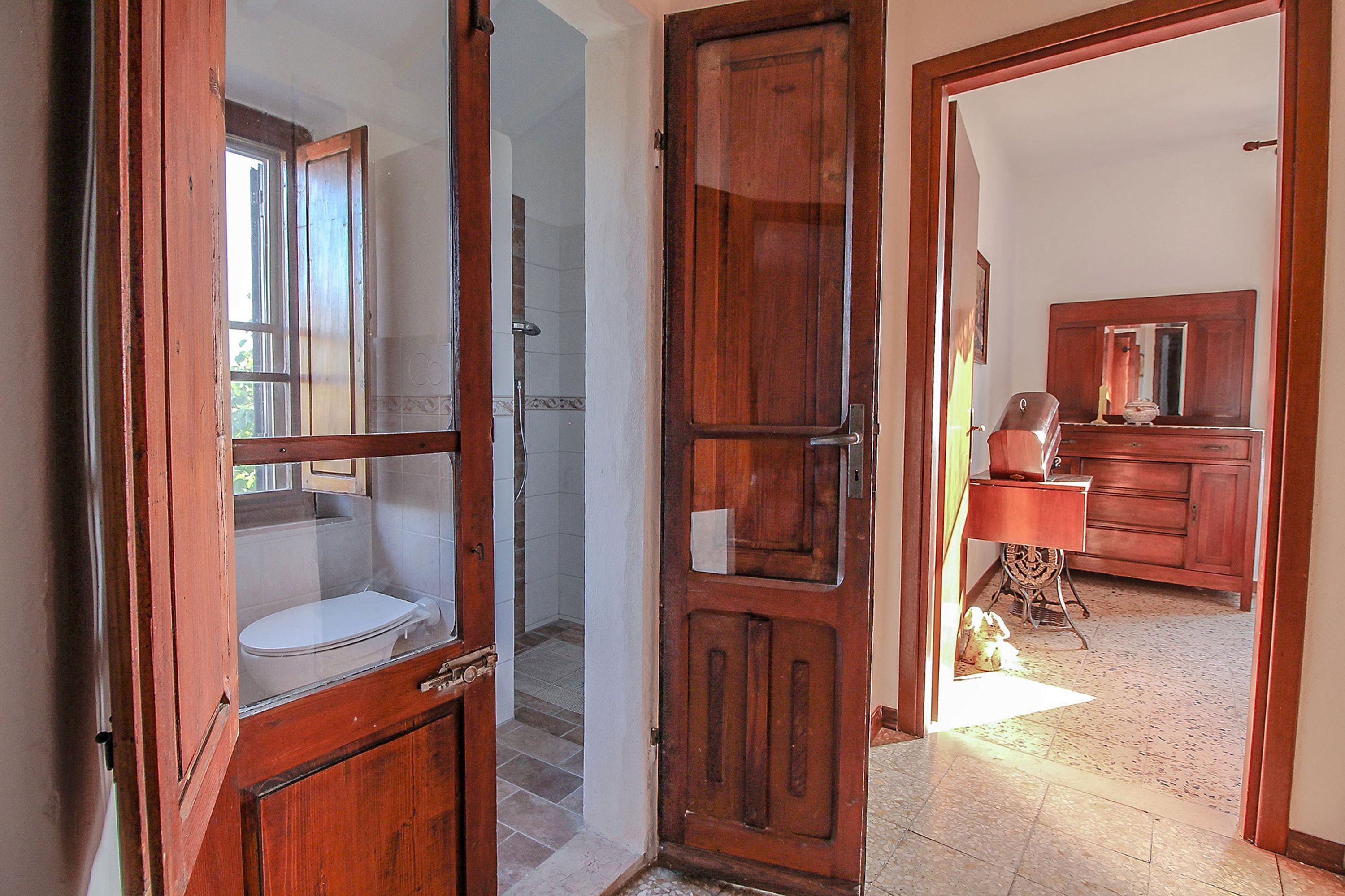 An open wooden door leading to a bathroom with a toilet and a shower.