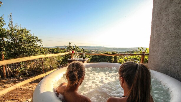 Two people in a hot tub with a wooden railing and a view of the landscape.
