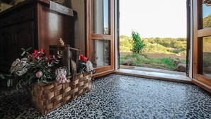 A room with a wooden cabinet, a woven basket of flowers, and a view of a green landscape through a glass door.
