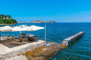 A seaside terrace with outdoor seating, a wooden pier, and a view of a distant island. - Le Grotte Villa Isola d Elba (Portoferraio)