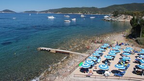 A beach with clear water, boats, and umbrellas.