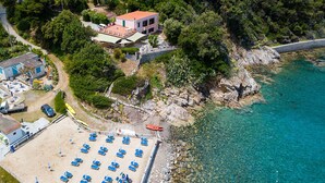 An aerial view of a coastal property with a beach, a building with a red roof, and a clear blue sea.
