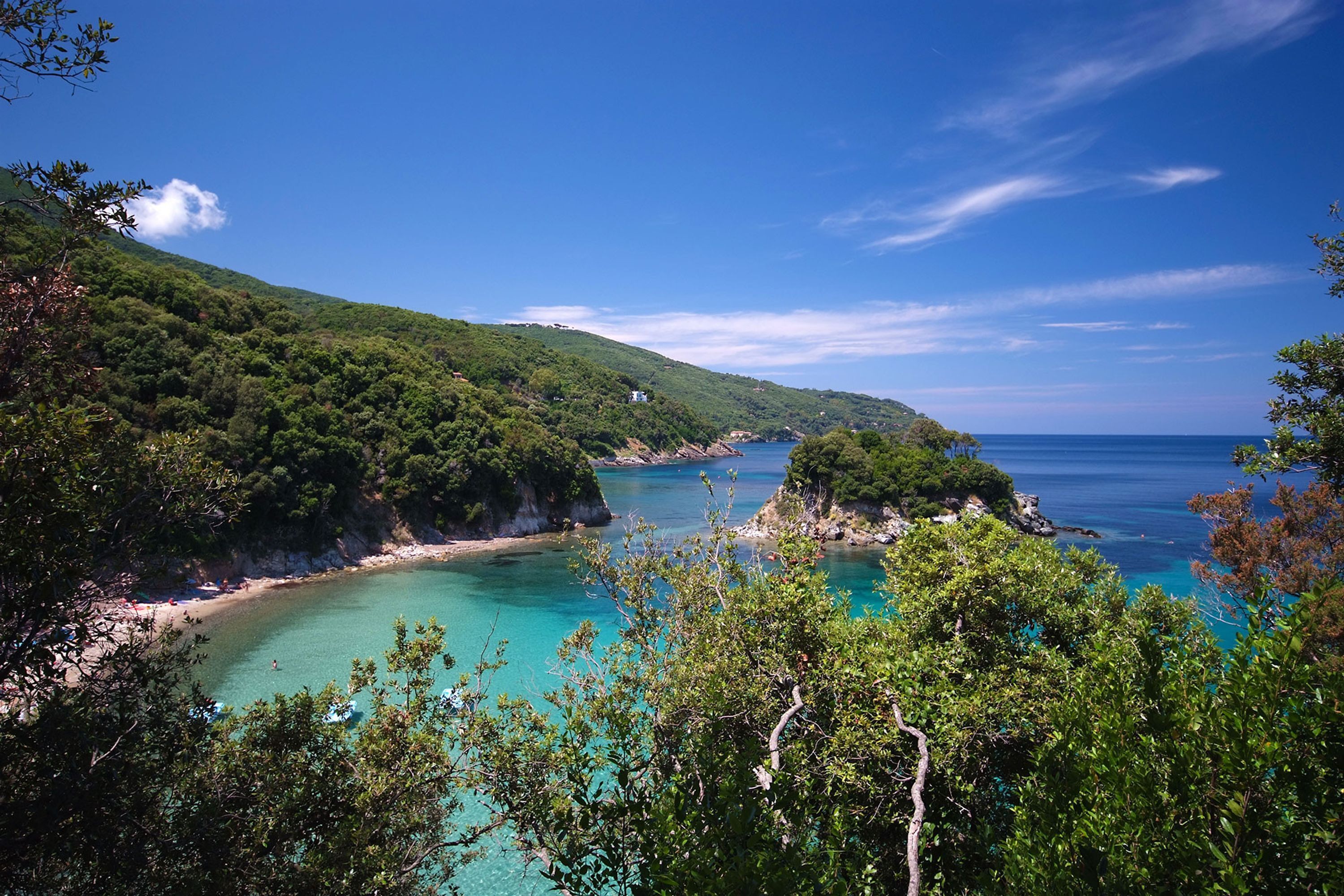 A coastal landscape with a clear view of a beach, lush green hills, and a calm sea.