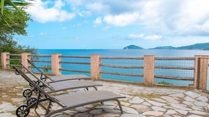 A stone-paved area with lounge chairs and a view of the sea.