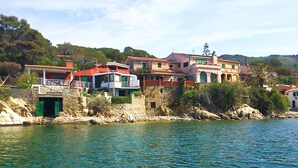 Un edificio costero con muro de piedra, puerta verde y balcón con vista al agua.