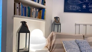 Un dormitorio ordenado con una estantería, un farol decorativo, una lámpara esférica, almohadas estampadas y un dibujo arquitectónico enmarcado en la pared.