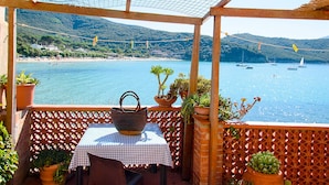 Una terraza con mesa y sillas, con vistas a una zona costera con barcos y vegetación.