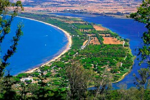 A coastal landscape with a beach, green hills, and a winding road.
