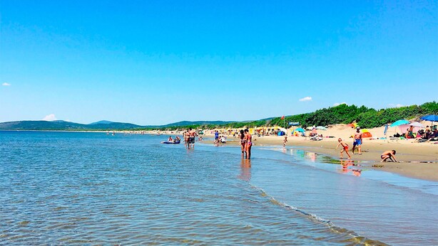 Una playa con aguas cristalinas, gente y sombrillas.