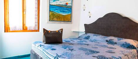 Ein Schlafzimmer mit einem Bett, einem Strandbild, einem Fenster mit Spitzenvorhängen und einem blau gefliesten Boden.