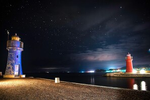 Deux phares se dressent au bord d’une étendue d’eau calme, la nuit, sous un ciel étoilé.