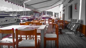 Un espace extérieur aménagé pour les repas, avec des tables et des chaises, donnant sur une marina où sont amarrés des bateaux.