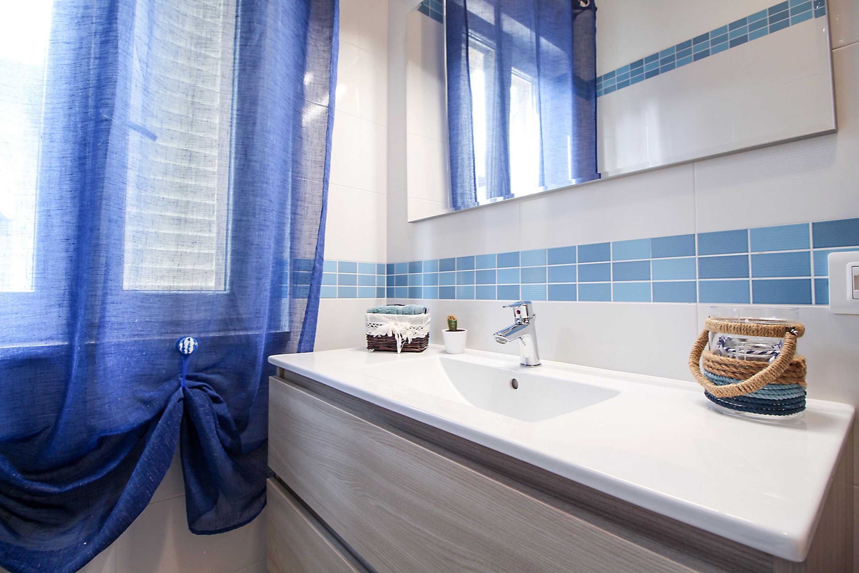 Un baño con un lavamanos blanco, paredes de azulejos azules, un espejo y una cortina azul.