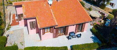 A two-story building with a red-tiled roof, a paved patio with outdoor seating, and a small garden area.