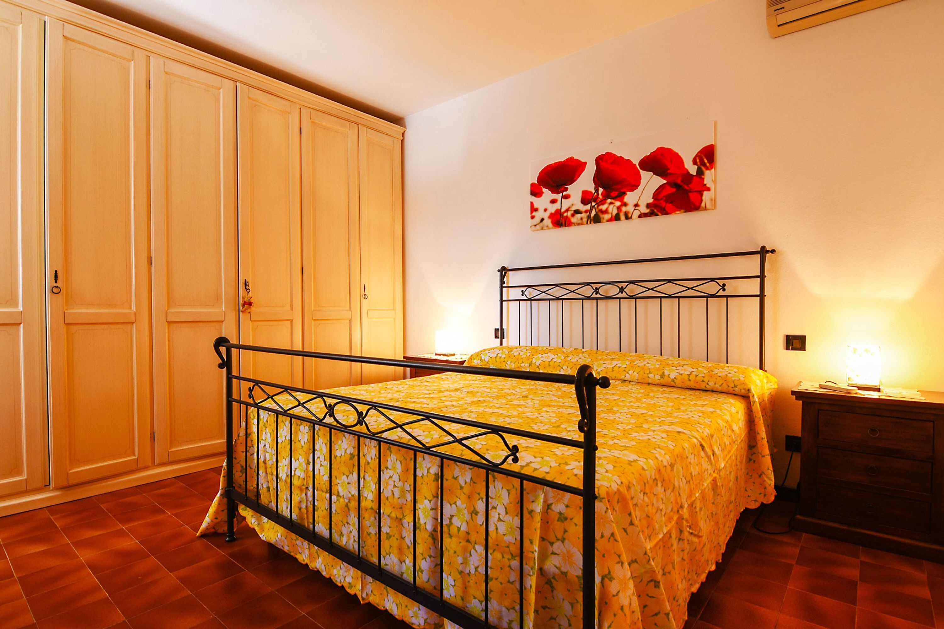 A bedroom with a bed, wooden wardrobe, and a wall-mounted artwork.