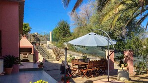 An outdoor patio with a table and chairs, surrounded by potted plants and a staircase leading to a building.