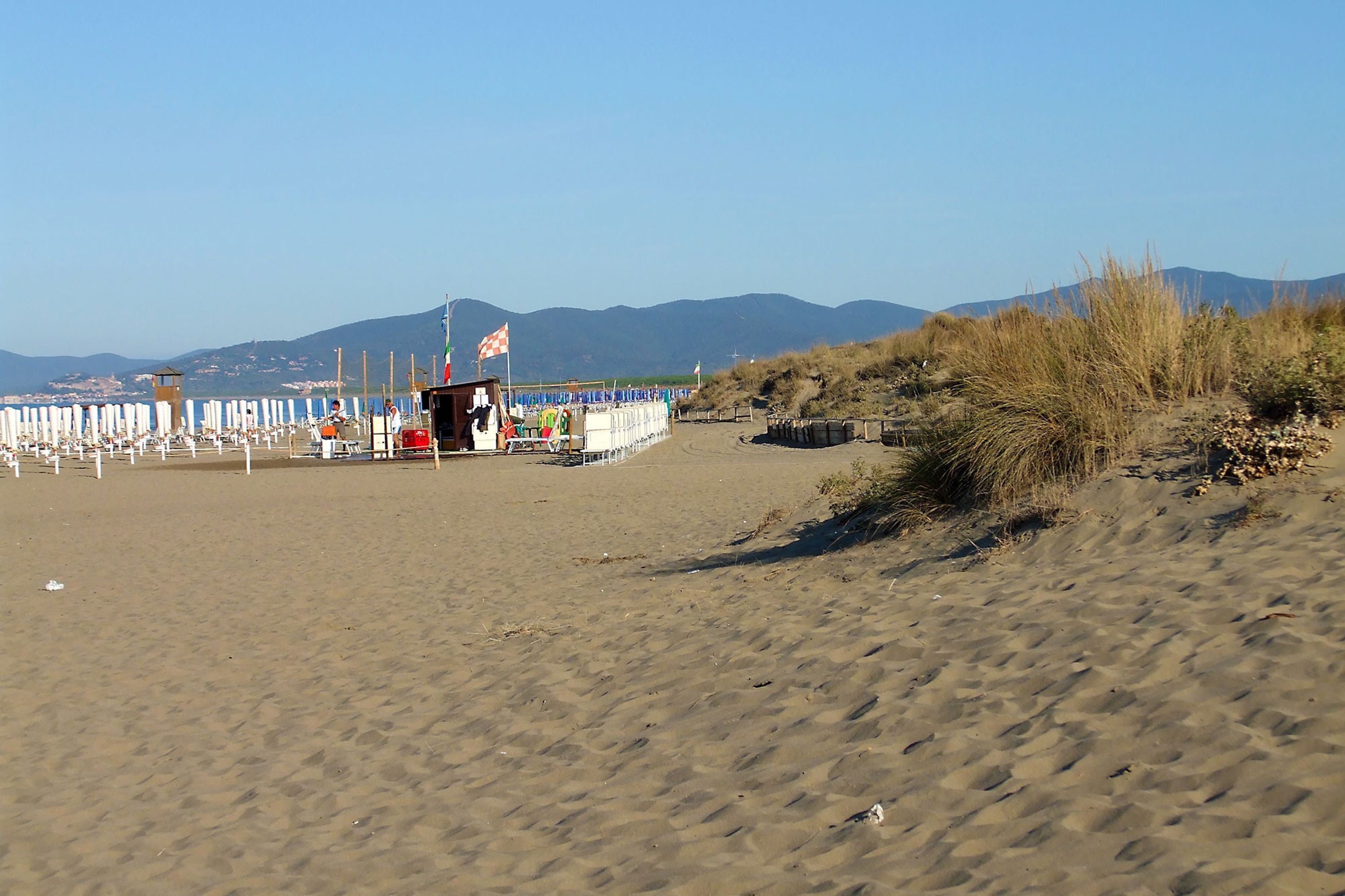 A beach with a lifeguard tower, umbrellas, and a flag.