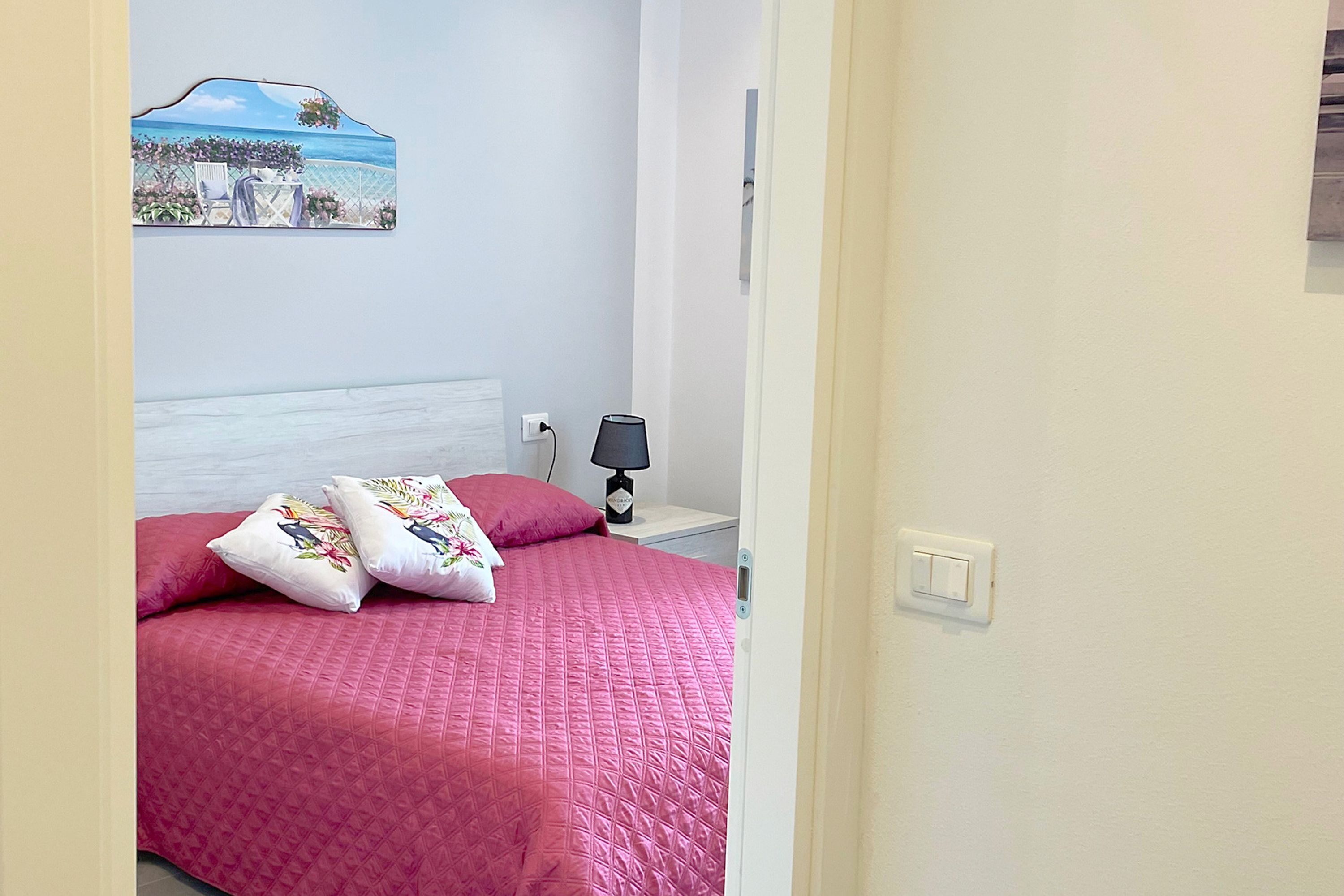 A bedroom with a bed, pillows, a nightstand, a lamp, and a wall-mounted painting.