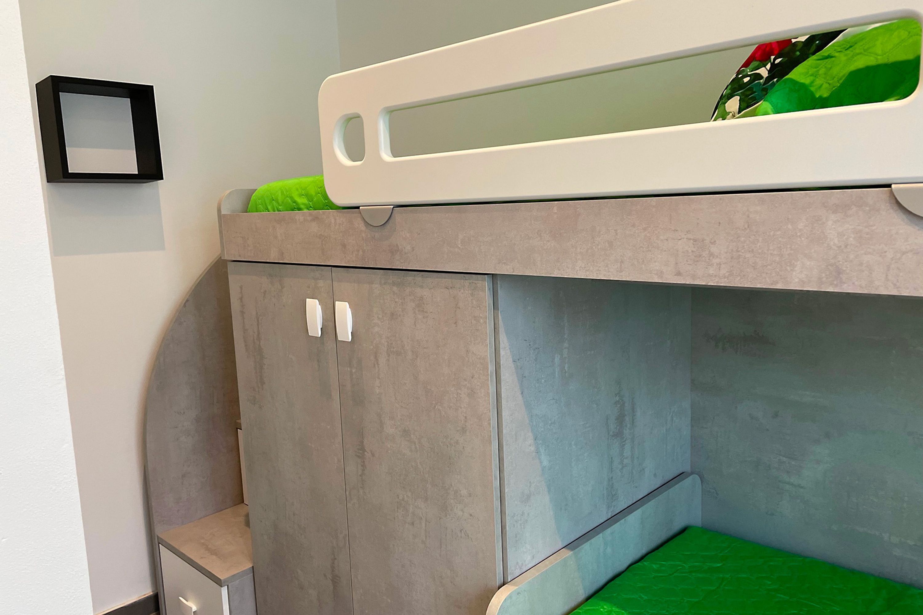 Una cama litera con colchón verde, un mueble pequeño y un cuadro en la pared.