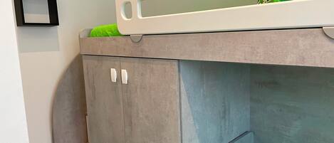 Una cama litera con colchón verde, un mueble pequeño y un cuadro en la pared.