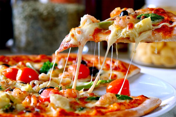 Primer plano de una pizza con varios ingredientes, entre ellos verduras y queso, que se levanta de un plato.