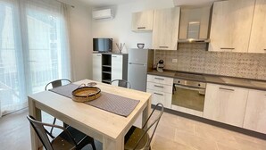 A modern kitchen with light wood cabinets, a built-in oven, and a dining area with a table and chairs. - Appartamento Malibu Vicino Alla Spiaggia (Grosseto)