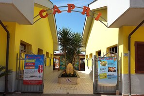 Entrada de un hotel con fachada amarilla, un letrero que dice "CAPRI" y dos carteles anunciando el bar y sus servicios.