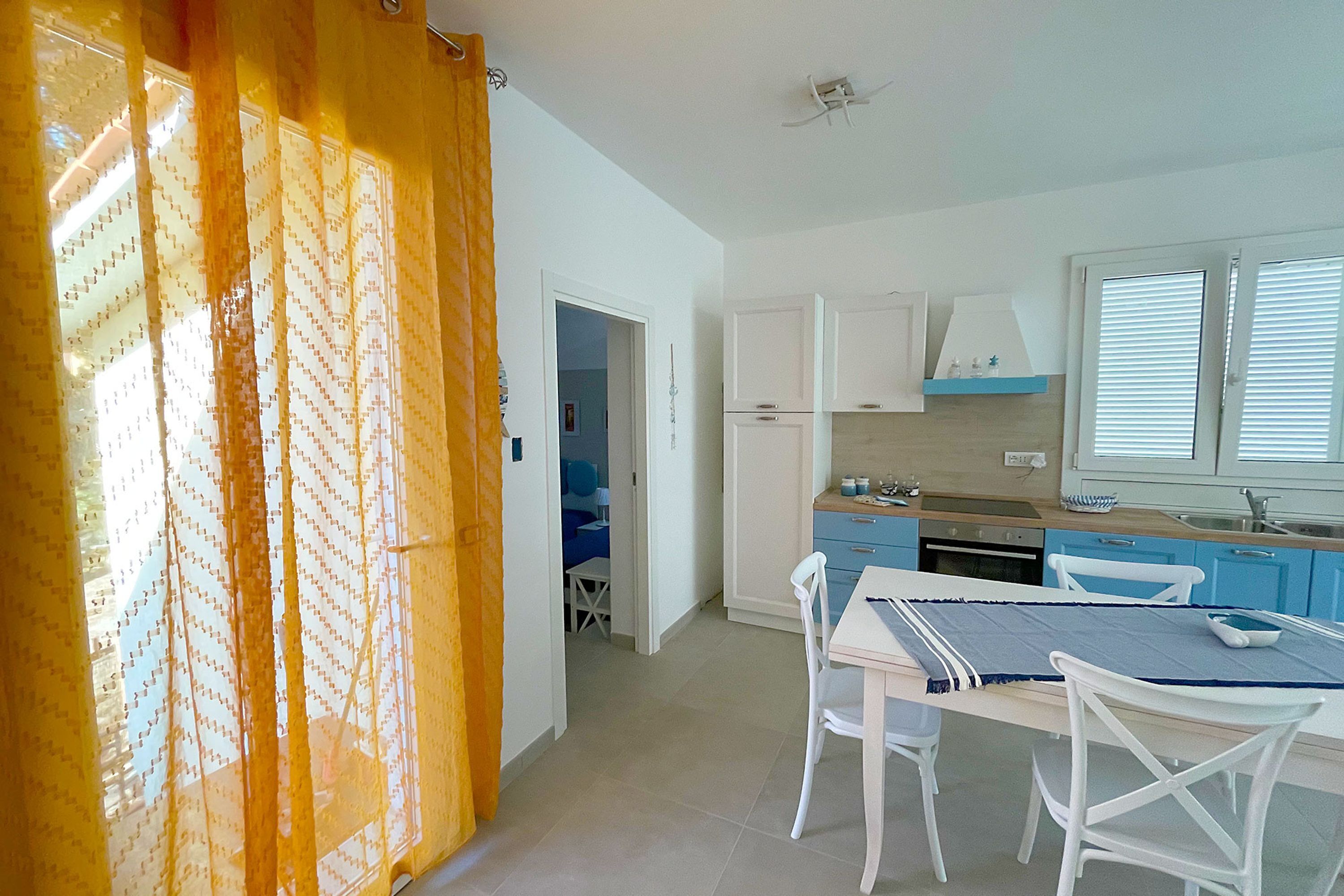 A kitchen with white cabinets, a dining table with chairs, and a window with blinds.
